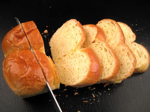 Une brioche est coupée en tranches épaisses sur le plan de travail et à l'aide d'un couteau