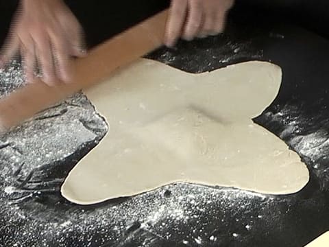 La pâte est abaissée sur la largeur et forme une croix, à l'aide d'un rouleau à pâtisserie et sur le plan de travail fariné