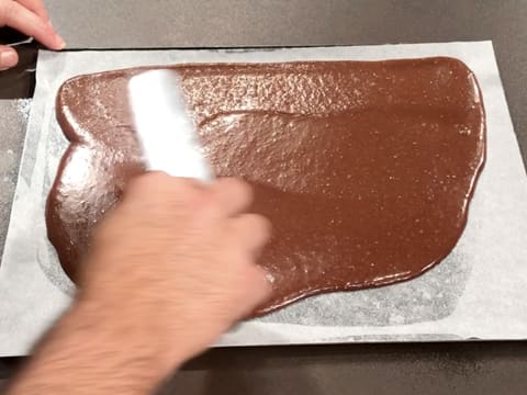 La pâte à biscuit chocolat est étalée sur la feuille de papier sulfurisé, à l'aide d'une spatule coudée