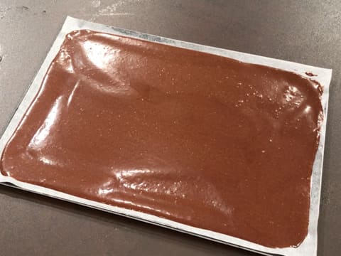 La pâte à biscuit chocolat est étalée sur toute la surface de la feuille de papier sulfurisé