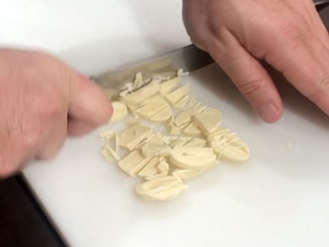 Du chocolat blanc est haché au couteau sur une planche à découper