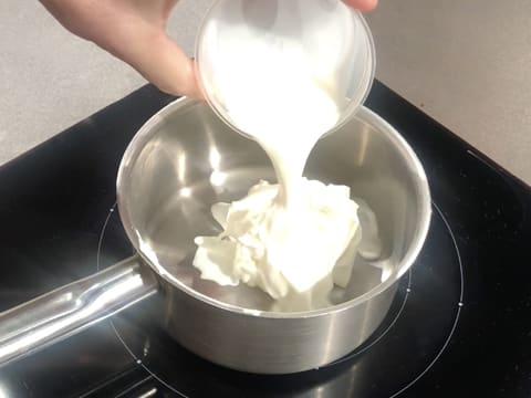 Ajout du lait sur le fromage blanc dans la casserole qui est sur la plaque de cuisson