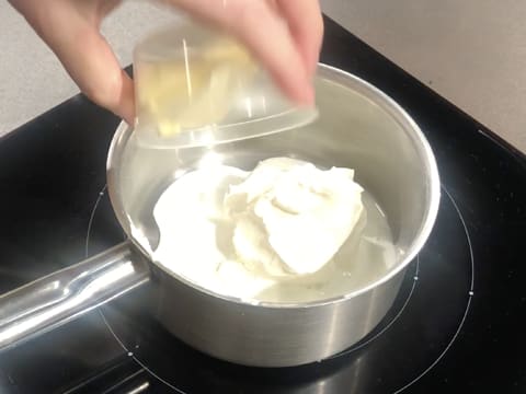 Ajout du beurre sur le lait et le fromage blanc dans la casserole qui est sur la plaque de cuisson