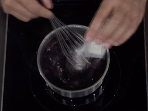 La pectine et le sucre sont versés sur la purée de myrtille dans la casserole, tout en étant mélangés avec un fouet