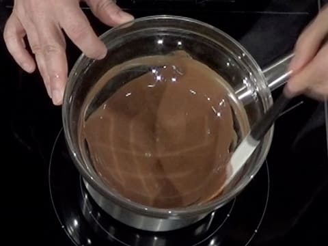 Mélange du chocolat au lait et du beurre de cacao Mycryo fondus avec la spatule maryse dans le saladier qui est placé sur un bain-marie