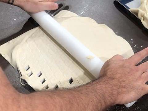 La pâte feuilletée est étalée et écrasée sur le découpoir à décor pour tourte, à l'aide du rouleau à pâtisserie