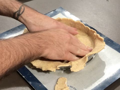 La pâte sablée à la noix de pécan est foncée dans le cercle à tarte en inox qui est posé sur un tapis de cuisson en silicone