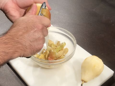 Les poires sont pelées à l'aide d'un éplucheur au dessus d'un bol en verre posé sur une planche à découper