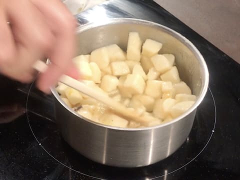 Mélange des gros morceaux de poires dans le beurre et le sucre fondus dans la casserole, à l'aide d'une spatule