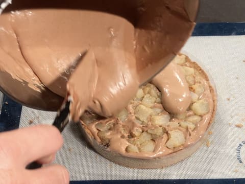 La mousse légère chocolat est versée sur les morceaux de poires rôties piqués dans la mousse sur le fond de tarte