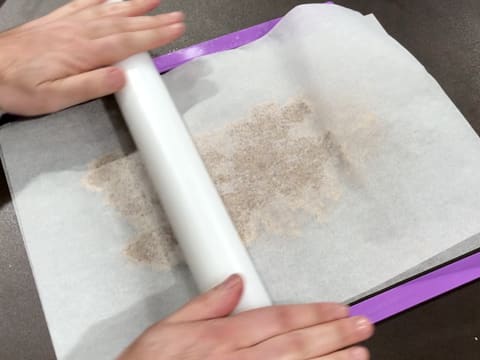 La pâte à streusel recouverte de la feuille de papier sulfurisé, est abaissée sur la longueur à l'aide d'un rouleau à pâtisserie et de deux réglettes à niveler positionnées de chaque côté de la pâte