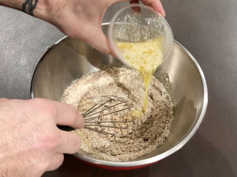 Le beurre fondu est versé sur les poudres dans le cul de poule, tout en étant incorporé au fouet