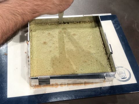 La lame d'un couteau est passée entre le biscuit thé matcha et le cadre inox qui sont posés sur le tapis de cuisson en silicone