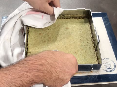 Le cadre inox est retiré du biscuit thé matcha avec un torchon de cuisine