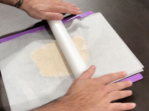 La pâte à streusel amande est abaissée de façon verticale au rouleau à pâtisserie, entre deux feuilles de papier sulfurisé et entre deux réglettes à niveler violettes