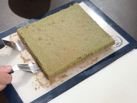 Deux grandes spatules métalliques coudées sont glissées sous le biscuit thé matcha