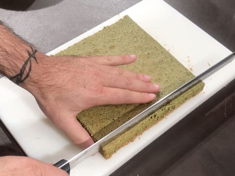 Un côté du biscuit thé matcha est arasé à l'aide d'un couteau-scie à génoise sur une planche à découper