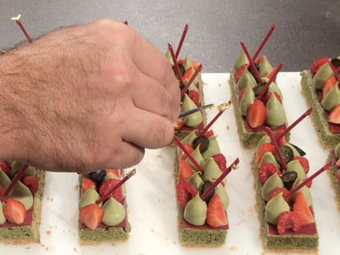 Une pointe de feuille d'or est déposée sur chaque goutte pochée sur les bâtonnets en chocolat inspiration framboise, à l'aide d'une pince à dresser