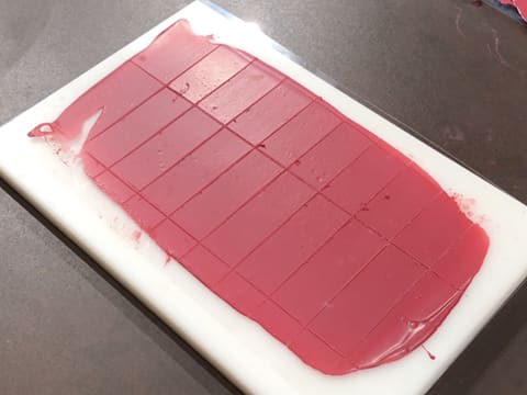 Obtention des plaquettes de chocolat taillées dans la bande de chocolat inspiration framboise cristallisé sur la feuille guitare posée sur une planche à découper