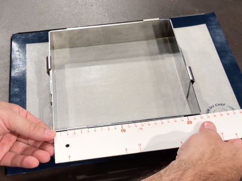 Un cadre à pâtisserie extensible mesurant 22 cm de côté, est placé sur une plaque à pâtisserie recouverte d'un tapis de cuisson en silicone