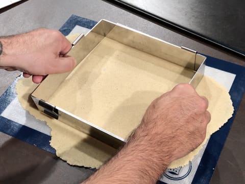 Le cadre à pâtisserie extensible est placé sur le streusel amande qui est abaissé sur le tapis de cuisson en silicone
