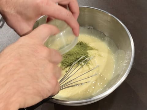 Ajout du thé matcha en poudre sur la crème au chocolat blanc dans le cul de poule posé sur le plan de travail