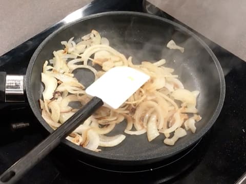 Les oignons sont en train de cuire et de colorer dans la poêle, avec une spatule maryse posée dessus